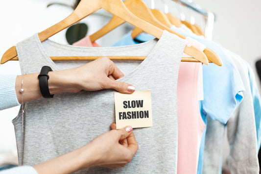 A person holding slow fashion label on top of multi coloured cotton t-shirts
